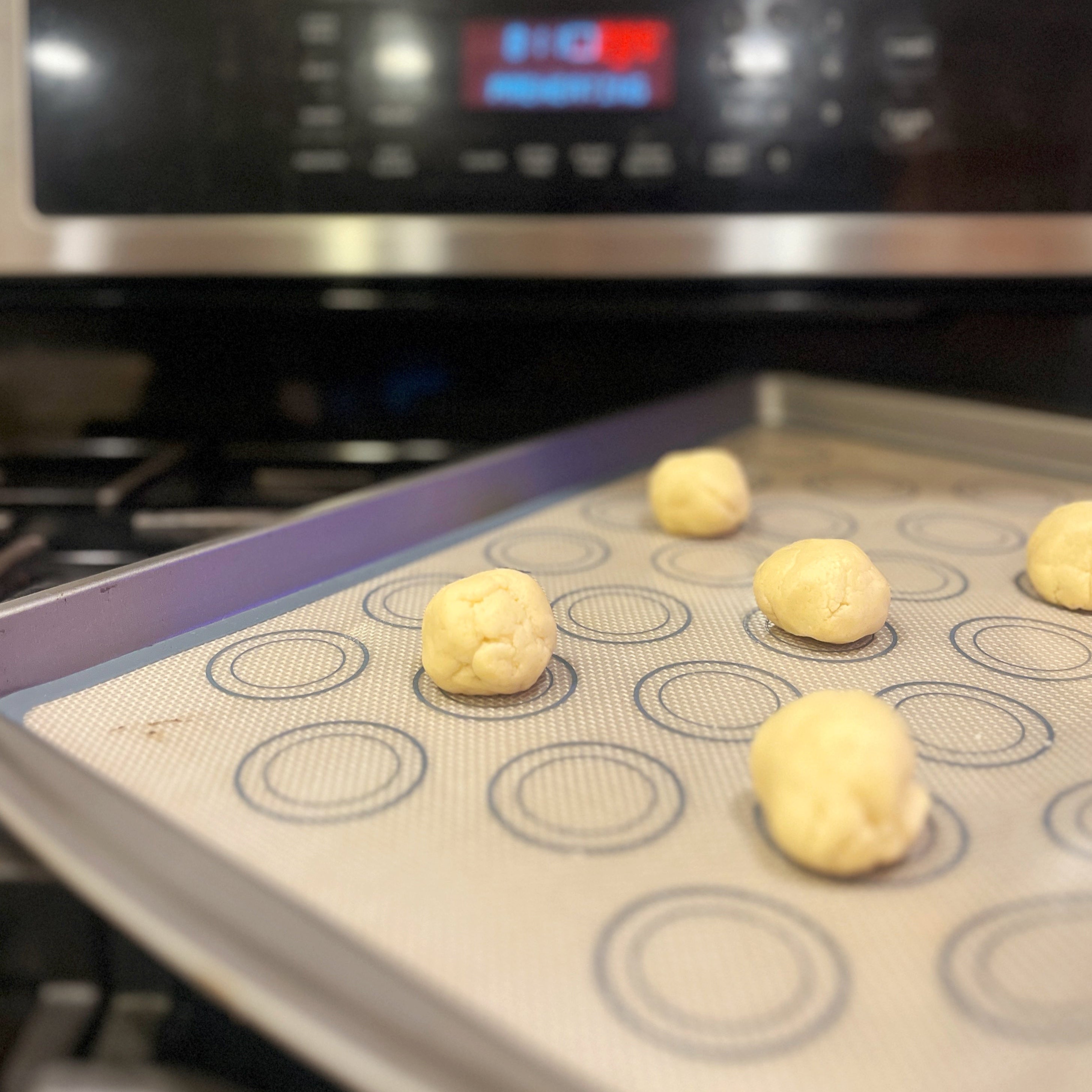 Balls of dough on a baking sheet in front of an oven.